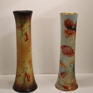 May include: Two tall ceramic vases with floral designs. The vase on the left has a brown base and a yellow body with red poppy flowers. The vase on the right has a white base and a light blue body with red poppy flowers.