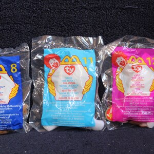May include: Three Ty Beanie Babies in their original McDonald's packaging. The blue package features "Nuts the Squirrel", the light blue package features "Wook the Husky", and the pink package features "Cip the Cat".
