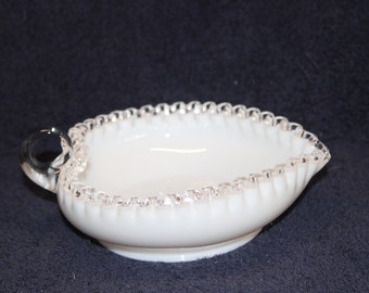 May include: A white milk glass bowl with a silver trim and a clear glass handle. The bowl is shaped like a heart and has a scalloped edge.