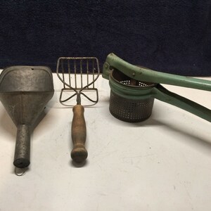 May include: Three vintage kitchen tools: a green metal potato masher, a green metal funnel, and a wooden handled wire whisk.