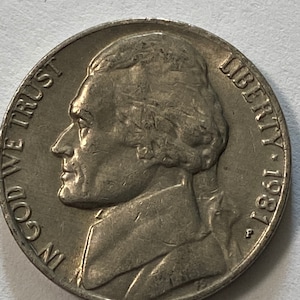 May include: A silver US nickel coin with the profile of Thomas Jefferson on the obverse. The coin reads "IN GOD WE TRUST" and "LIBERTY 1967" around the edge. The coin has a "P" mint mark.