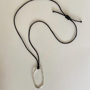 May include: A silver oval pendant necklace with a textured surface, hanging from a black cord.