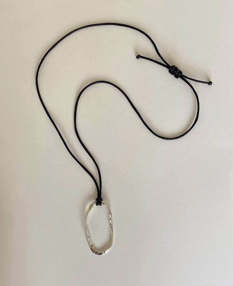May include: A silver oval pendant necklace with a textured surface, hanging from a black cord.