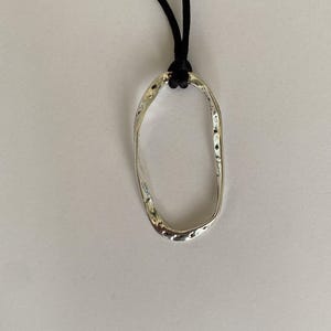 May include: A silver oval pendant necklace with a textured surface, hanging from a black cord.