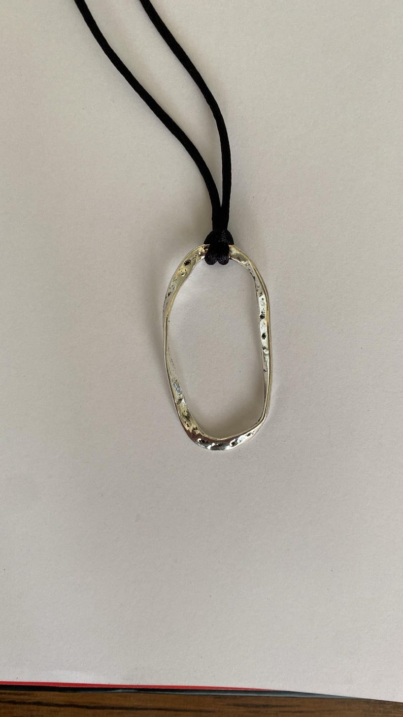 May include: A silver oval pendant necklace with a textured surface, hanging from a black cord.