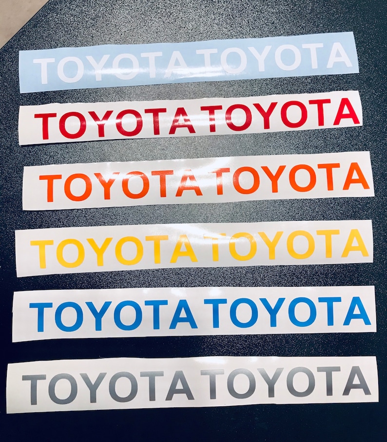 May include: Six rectangular decals with the word "TOYOTA" in various colours: light blue, red, orange, yellow, blue, and grey. The decals are arranged vertically. Each decal is a different colour.
