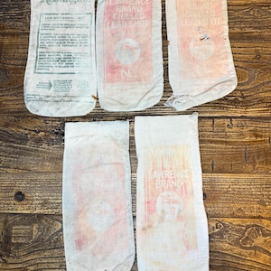 May include: Five vintage lead shot bags. The bags are white with red and black text. One bag reads "Remington" and includes a warning label. Other bags display "Lawrence Brand Chilled Lead Shot". The bags are on a wooden surface.