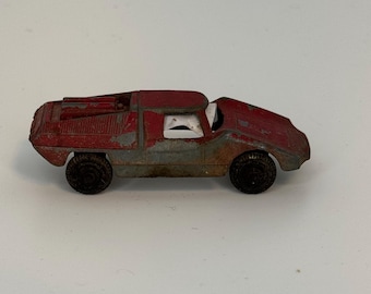 May include: A vintage red toy car with black wheels. The car has a weathered appearance, with visible signs of wear and tear on its red paint. The car's design features a low profile and a distinctive shape, suggesting a classic or retro style.