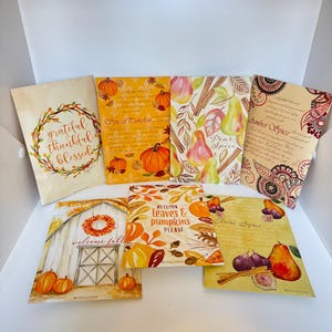 May include: A collection of autumn-themed paper goods with illustrations of pumpkins, pears, and leaves. The designs include text such as "Grateful, Thankful, Blessed," "Spiced Pumpkin," and "Welcome Fall." The colour scheme is warm, with oranges, yellows, and browns.