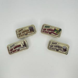May include: Four rectangular vintage lip balm tins with illustrations and text. The tins feature images of root beer, pineapple, coffee, and Miss Pepper. The text reads "Vintage Moisturizing Lip Licking Lip Balm."