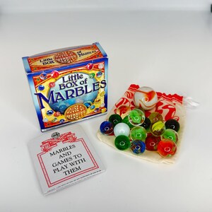 May include: A "Little Box of Marbles" game set. The box is blue and red with the text "Little Box of Marbles". A small bag of colorful glass marbles and a booklet titled "Marbles and Games to Play With Them" are also included.