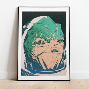 May include: A framed art print featuring a stylized illustration of a reptilian alien with green and tan skin. The artwork has a textured, grainy appearance and is set against a dark background. The alien has yellow eyes and is wearing a blue and white helmet.