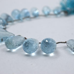 May include: A strand of light blue aquamarine gemstone beads. The beads are faceted and have a teardrop shape. The beads are strung on a silver wire.