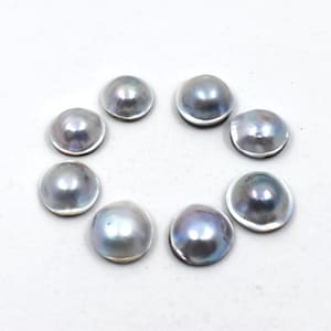 Peut inclure: Sept perles circulaires en forme de dôme disposées en cercle. Chaque perle présente une surface lisse et lustrée avec une finition gris métallique aux reflets bleutés irisés, réfléchissant la lumière avec un éclat doux sur leurs sommets.