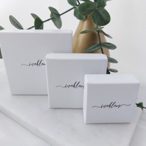 K&ouml;nnte beinhalten: Drei wei&szlig;e quadratische Boxen mit dem Wort "irahlan" in Kursivschrift auf jeder Box. Die Boxen sind &uuml;bereinander gestapelt, wobei die gr&ouml;&szlig;te Box unten und die kleinste Box oben liegt.