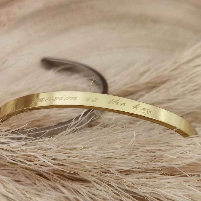Op de afbeelding: Een gouden armband met de inscriptie "Passion is the key" gegraveerd op de voorkant.
