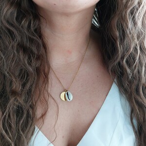 Op de afbeelding: Een gouden ketting met een kleine gouden schijf en een hanger van een kauri schelp.