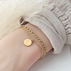 Op de afbeelding: Een gouden kettingarmband met een delicate halve maan bedel. De armband is gelaagd met een dikkere curb-ketting.