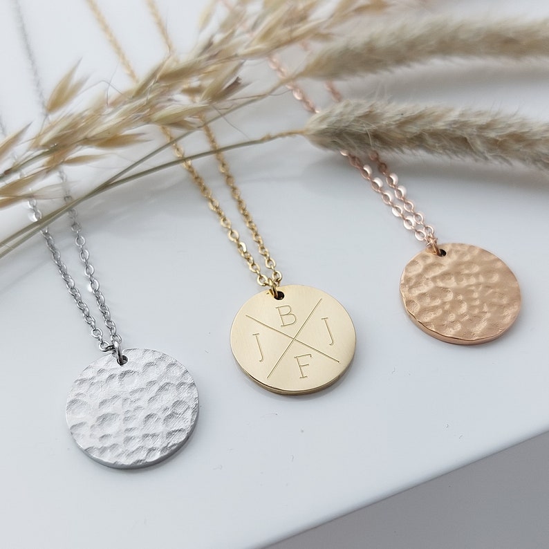 May include: Three necklaces with round, hammered metal pendants. The pendant on the left is silver, the middle pendant is gold with the initials "JBF" engraved on it, and the pendant on the right is rose gold.
