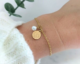 May include: Gold chain bracelet with a small pearl charm and a round charm with the letters "SGB" and the number "22" engraved on it.
