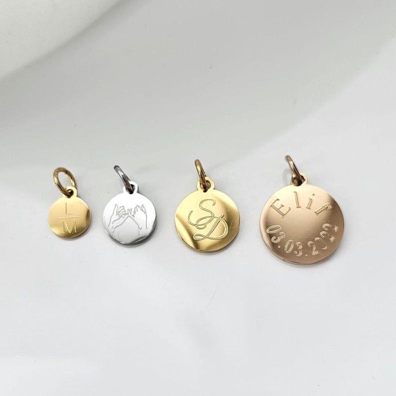 K&ouml;nnte beinhalten: Vier runde Anh&auml;nger in Gold, Silber und Ros&eacute;gold mit verschiedenen Gravuren. Die Anh&auml;nger zeigen die Buchstaben "LM", zwei H&auml;nde, die ein Pinky-Versprechen machen, die Buchstaben "SD" und den Namen "Elif" mit dem Datum "03.03.2023".