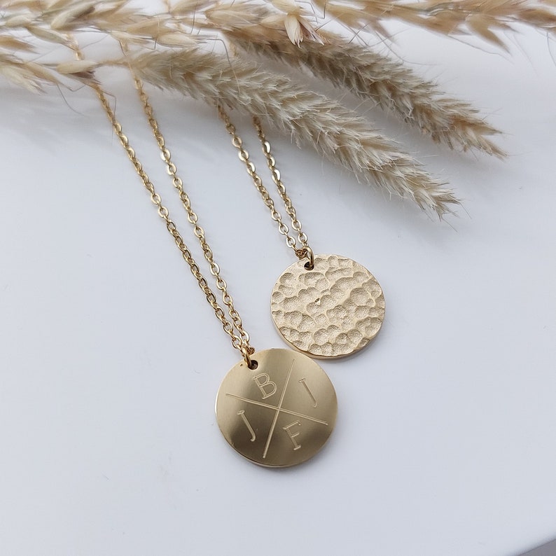 May include: Two gold necklaces with circular pendants. One pendant has a hammered texture, the other has an engraved design with the letters "J", "B", "E", and "I" arranged in a cross pattern.