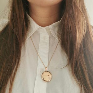 May include: A gold chain necklace with a round locket pendant.