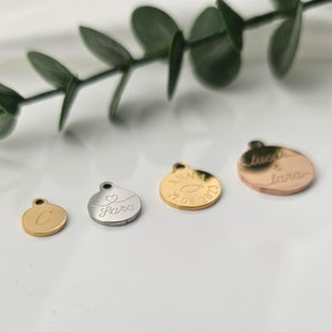 K&ouml;nnte beinhalten: Vier runde Metall-Anh&auml;nger mit verschiedenen Gravuren. Die Anh&auml;nger sind golden, silbern und ros&eacute;gold. Die Gravuren beinhalten "Sara", "Anna 21.08.2023", "Lucas & Lara" und "C".