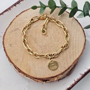 Könnte beinhalten: Ein goldenes Kettenarmband mit einem Anhänger, auf dem "Uuu" steht und zwei Hände ein Herz bilden.