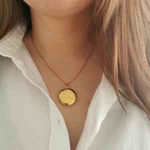 May include: A gold chain necklace with a round gold locket pendant.
