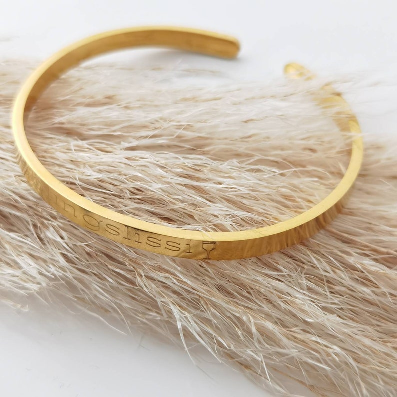 Op de afbeelding: Gouden armband met de inscriptie "I'm a little obsessed" en een wijnglasicoon.