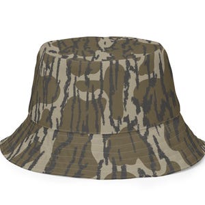 May include: A bucket hat with a camouflage pattern in shades of olive green, tan, and dark gray. The hat has a wide brim and a rounded crown. The camouflage design is made up of irregular shapes and lines.