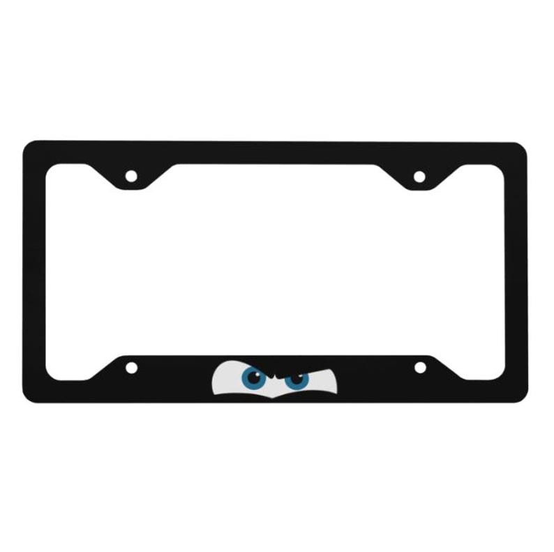 Puede incluir: Un marco de matr&iacute;cula rectangular negro que presenta un gr&aacute;fico de dos ojos estilizados y entrecerrados con iris azules y escler&oacute;tica blanca colocados en la parte inferior central del marco. El marco incluye cuatro orificios de montaje.