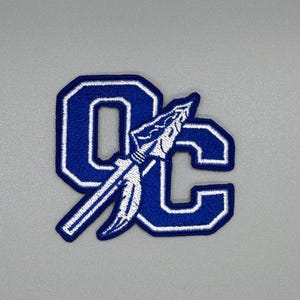 May include: Blue and white embroidered patch with the letters "OC" and a white spear design.