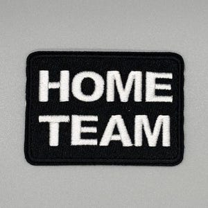 May include: Black embroidered patch with white text that reads "HOME TEAM".