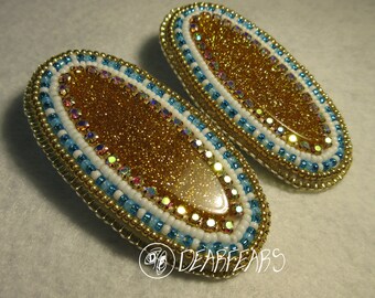 May include: A pair of oval-shaped earrings with a gold glitter background and a white and blue beaded border.