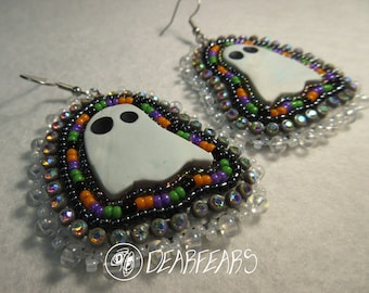 May include: A pair of beaded earrings with a white ghost charm. The earrings are made with black, orange, green, and purple beads, and clear iridescent beads. The earrings are signed "Dearfears".