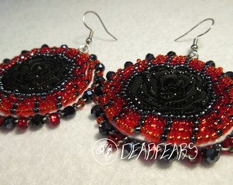 May include: A pair of beaded earrings with a black rose design. The earrings are made with red, black, and silver beads. The earrings are hanging from silver hooks.