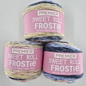 May include: Three Premier Sweet Roll Frostie yarn skeins. Each skein is wrapped with a pink label that reads "SWEET ROLL FROSTIE" and includes the measurements: 245 yds / 224 m, 5 oz / 140 g. The yarn colors include beige, blue, and cream.