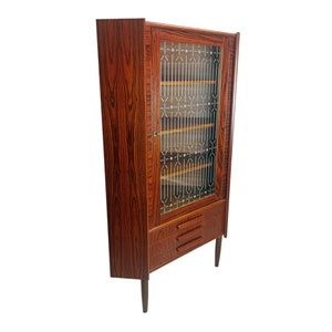 Könnte beinhalten: Ein Eck-Schrank mit einer Glastür und zwei Schubladen. Der Schrank ist aus dunklem Holz mit einer Holzmaserung. Die Glastür hat ein geometrisches Muster.