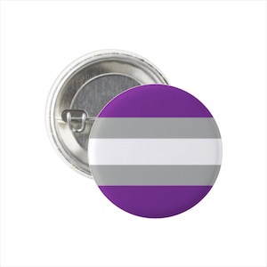 Könnte beinhalten: Ein runder Ansteckbutton mit dem Design der asexuellen Pride-Flagge. Die Flagge hat horizontale Streifen in Lila, Grau, Weiß und Grau. Der Button hat eine Metallrückseite mit Sicherheitsnadelverschluss.