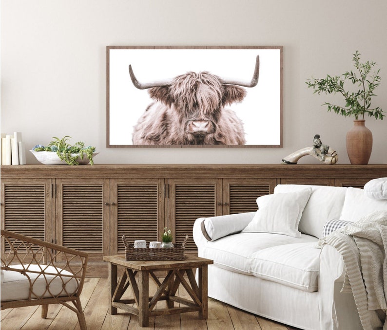 May include: A framed print of a Highland cow with long, shaggy brown fur and large horns. The cow is looking directly at the camera with a serious expression. The background is white.