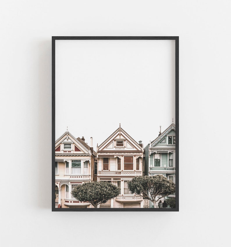 Puede incluir: Una impresi&oacute;n art&iacute;stica enmarcada que muestra tres casas de estilo victoriano en San Francisco. Las casas est&aacute;n pintadas en tonos rosa claro, crema y azul p&aacute;lido, con detalles arquitect&oacute;nicos intrincados, techos a dos aguas y dos &aacute;rboles verdes.