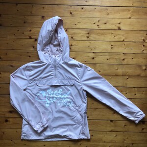 May include: A light pink hooded jacket with a white logo that says "Free & Wild" on the front. The jacket has a zip closure and two pockets.