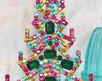 Op de afbeelding: Een kleurrijke kerstboomtopper gemaakt van strass en groene edelstenen. De boom is versierd met roze, blauwe, groene, oranje en gele strass.