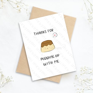 May include: A white card with a brown cartoon pudding with a smiling face and the text "Thanks for pudding up with me".