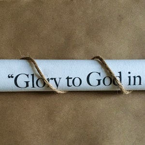 May include: A white scroll with the text "Glory to God in" written in black ink. The scroll is tied with twine and has wooden dowels at each end.