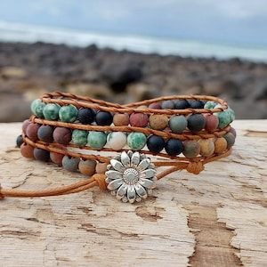 May include: A multi-strand wrap bracelet with brown leather cord and colourful gemstone beads. The bracelet features a silver sunflower charm.