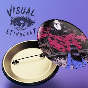 May include: A round button with a black and white illustration of a woman with long black hair standing in front of a red and pink sky. The text "VISUAL STIMULANT" is printed in black on a white background above the illustration.