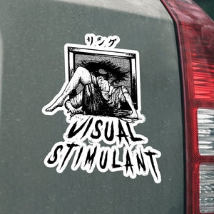 May include: A white sticker with a black and white illustration of a woman in a window. The text "VISUAL STIMULANT" is below the illustration. The sticker is on the back of a gray car.